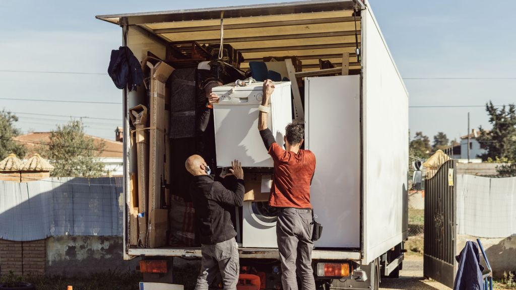 two movers loading an appliance into the back of a moving truck