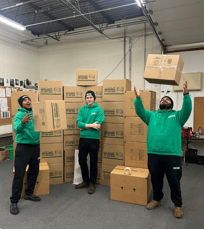 a group of three Good Stuff movers, tossing boxes in a room