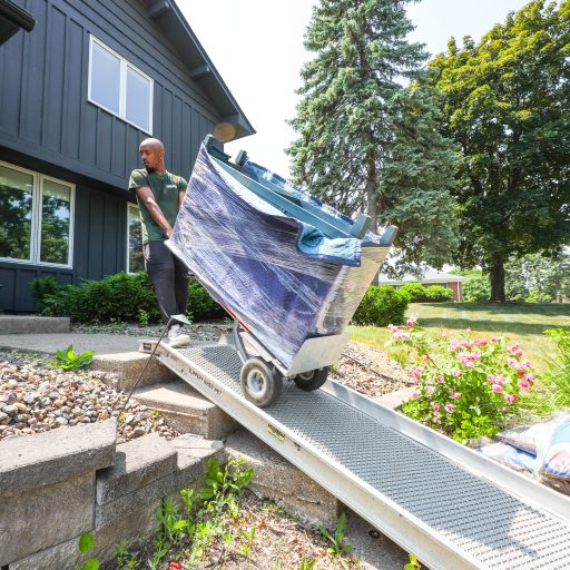 Cottage Grove movers using a ramp over front steps, a Good Stuff Moving crew member wheeling a wrapped sofa down on a dolly